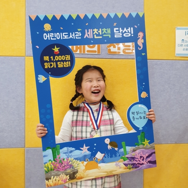 어린이도서관 “세상을 바꿀 천 권의 책” 1호 달성자 한소윤 어린이가 메달을 목에 걸고 환하게 웃고 있다.